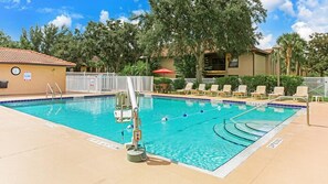 Relax by the pool surrounded by lounge chairs and umbrellas, with a fence and trees in the background.
