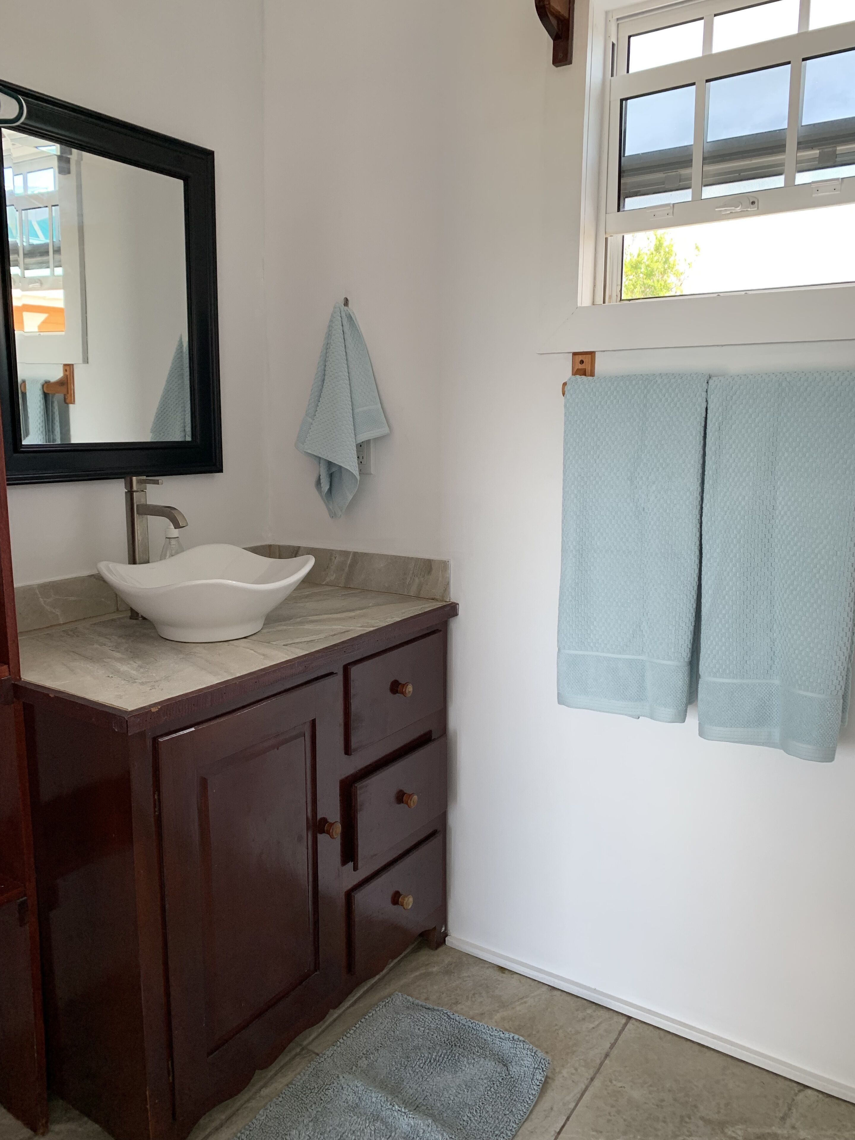 Un baño con un lavamanos blanco, tocador de madera oscura, un espejo y dos toallas colgadas en la pared.