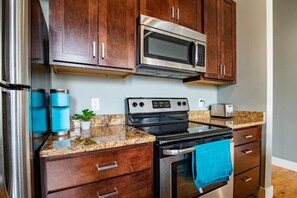 A kitchen with dark wooden cabinets, stainless steel appliances including a microwave and oven, a granite countertop, and a blue towel hanging on the oven handle.