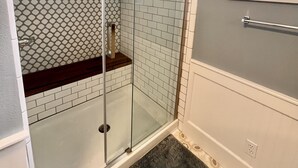 Een moderne badkamer met een glazen douchecabine, witte metrotegels en een houten wastafelmeubel.