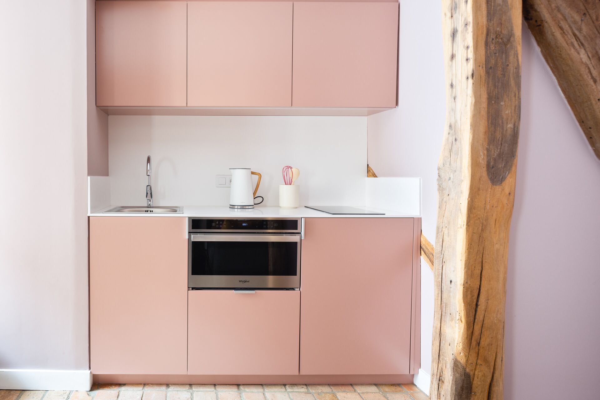Een kleine keuken met roze kastjes, een roestvrijstalen vaatwasser en een wit aanrecht.