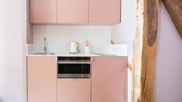 Een kleine keuken met roze kastjes, een roestvrijstalen vaatwasser en een wit aanrecht.