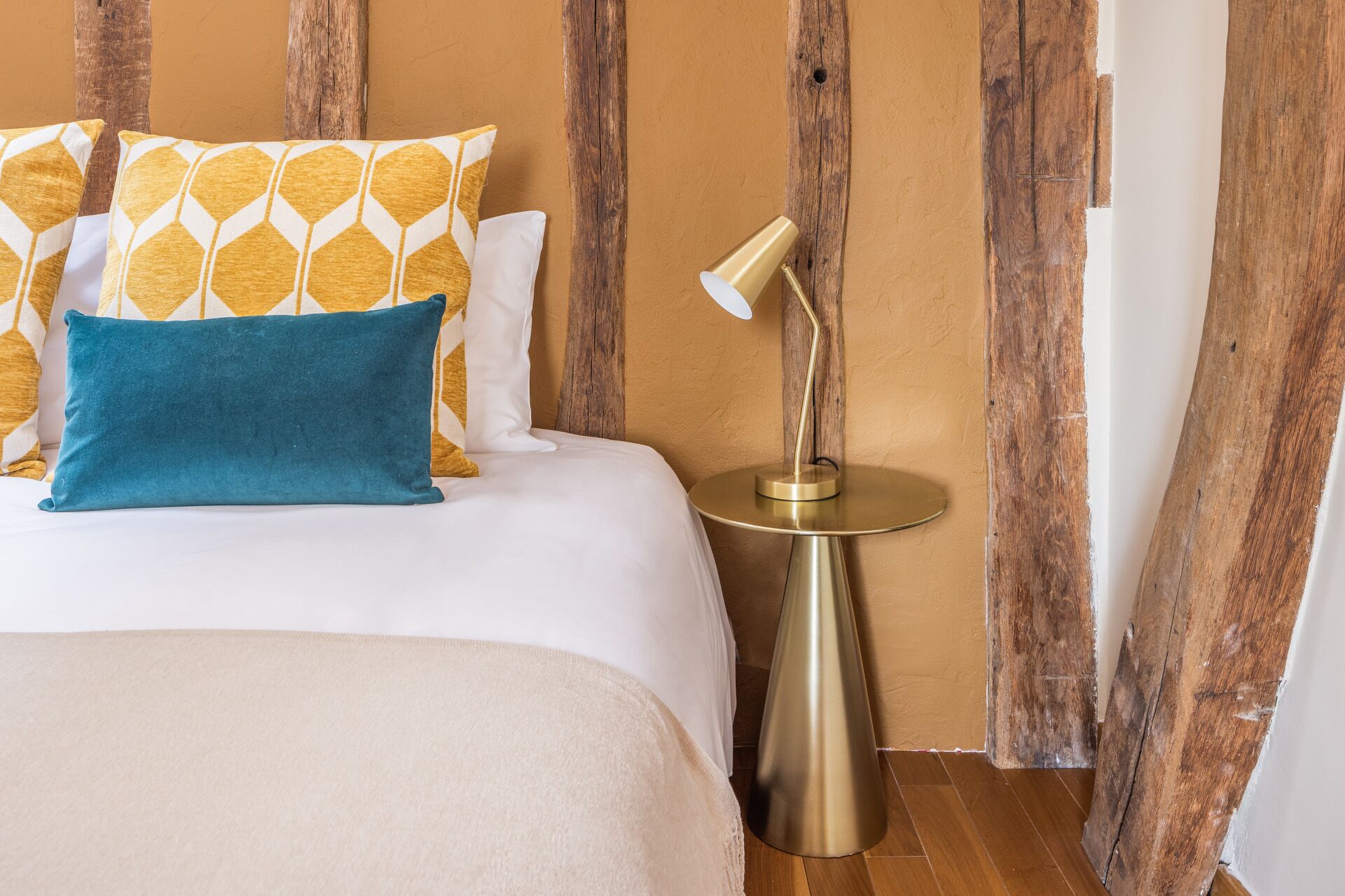 A bed with white and yellow patterned pillows, a teal pillow, and a gold lamp on a round table.