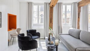 A modern living room with a grey sofa, black chairs, a small table with a bottle and glass, and a vase with flowers. - Break & Brut (Nogent-le-Roi)