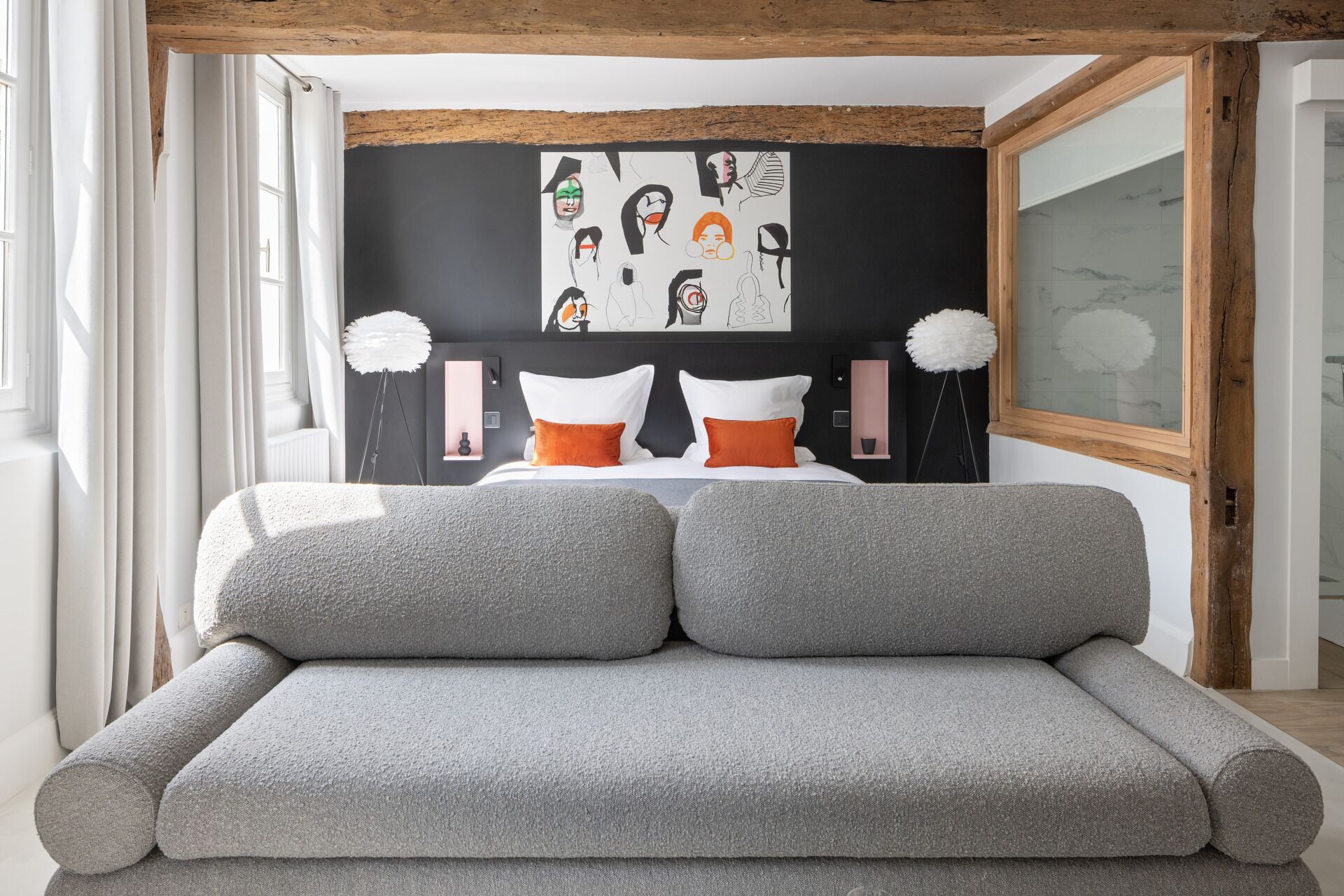 Ein modernes Schlafzimmer mit einer grauen Couch, einem Schwarz-Weiß-Kunstwerk an der Wand und einem großen Fenster mit Vorhängen.