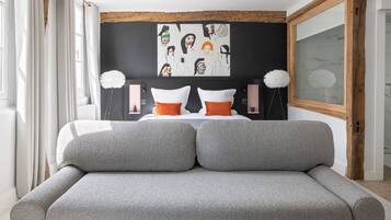 Ein modernes Schlafzimmer mit einer grauen Couch, einem Schwarz-Weiß-Kunstwerk an der Wand und einem großen Fenster mit Vorhängen.