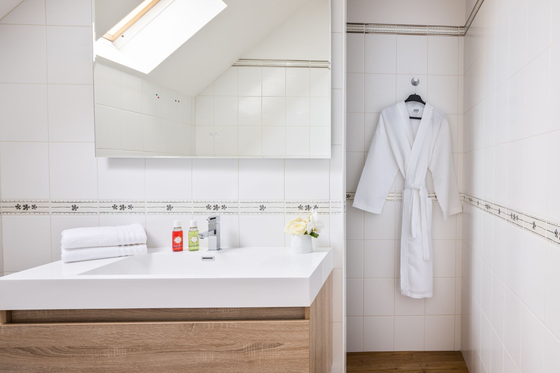 Un baño moderno con tocador blanco, espejo y bata colgada.