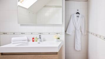 Un baño moderno con tocador blanco, espejo y bata colgada.