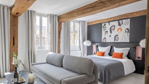 A modern bedroom with a grey sofa, a bed with orange pillows, and a black and white abstract art piece on the wall. - Break & Brut (Nogent-le-Roi)