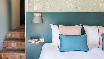 A bedroom with a bed, pillows, a nightstand, a lamp, and a wall with a botanical pattern.