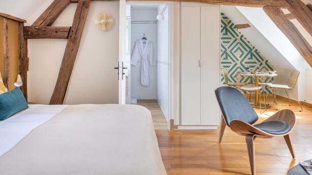 A bedroom with a large bed, a wooden ceiling, a bathroom with a shower, and a dining area with a table and chairs. - Break & Brut (Nogent-le-Roi)