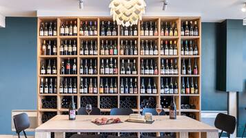 A modern dining area with a large wooden wine rack filled with various bottles, a table with chairs, and a decorative light fixture above.