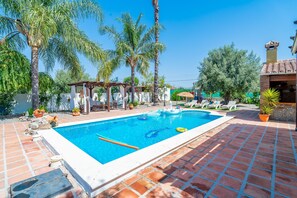 Una piscina con solárium de azulejos, palmeras y un pabellón.