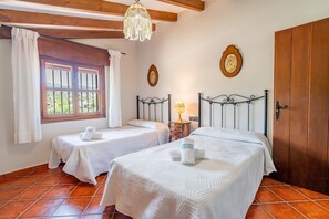Una habitación con dos camas, un armario de madera, una ventana con cortinas y una araña.