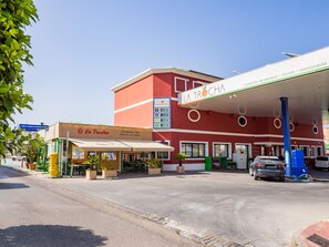 Eine Tankstelle mit einem roten Gebäude und einem weißen Vordach. Ein Auto ist unter dem Vordach geparkt.
