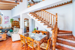 A spacious living area with a dining table, chairs, and a staircase with wooden balusters. - Cubo's Villa El Sauce de Coin / Private pool / BBQ / Air conditioning / Free Wi-Fi (Coín)