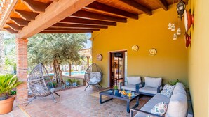 A covered patio with a sofa, chairs, and a table, a brick pillar, and a door leading to an interior space. - Cubo's Villa El Sauce de Coin / Private pool / BBQ / Air conditioning / Free Wi-Fi (Coín)