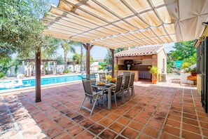 A patio with a table and chairs, a pool, and a covered area with a tiled roof.