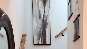 Eine Holztreppe mit Handlauf, ein an der Wand befestigtes abstraktes Gemälde und ein Spiegel.