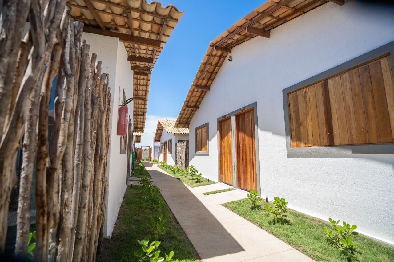 Un sentiero stretto costeggiato da edifici bianchi con porte e finestre in legno, che conduce a una zona riparata con tetto in tegole.