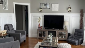 A living room with a flat-screen TV, grey sofas, a coffee table, and a patterned rug.