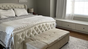 A bedroom with a large bed, a bench at the foot, a ceiling fan, and a window with curtains.