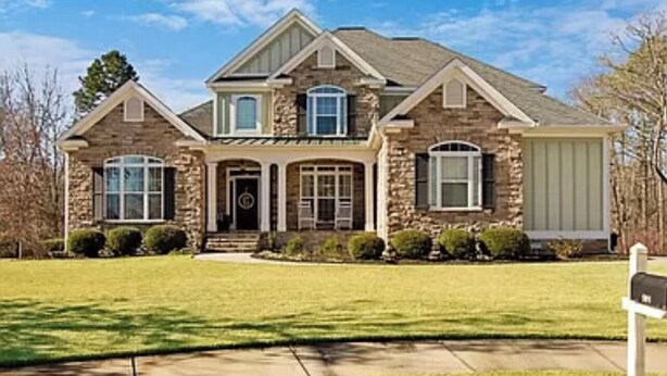 A two-story house with a stone facade, a front porch, and a well-maintained lawn.