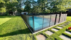 En pool med ett säkerhetsstaket runt om, omgiven av en välskött gräsmatta och ett trädäck.