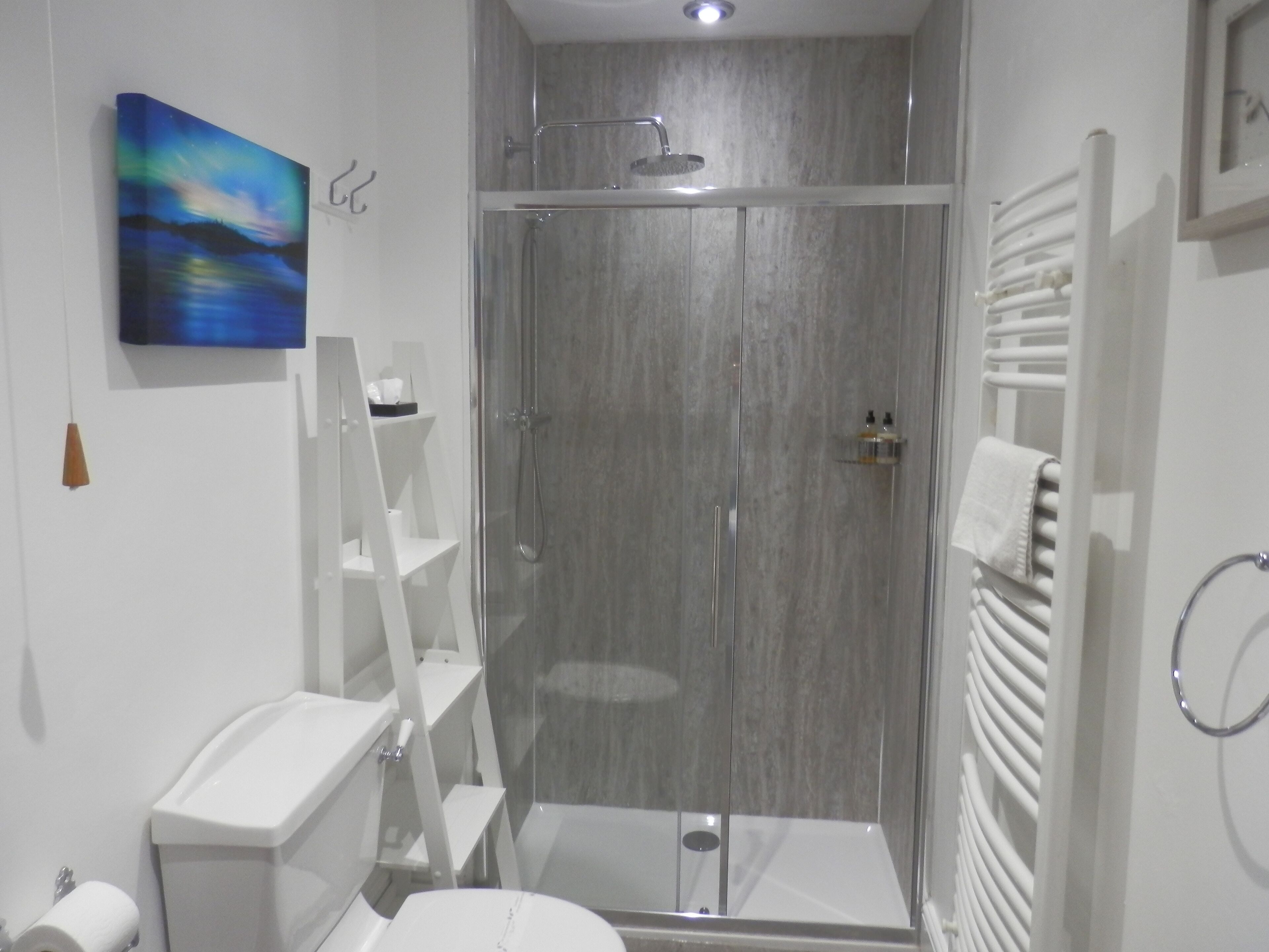 A modern bathroom with a glass-enclosed shower, white fixtures, and a painting on the wall.