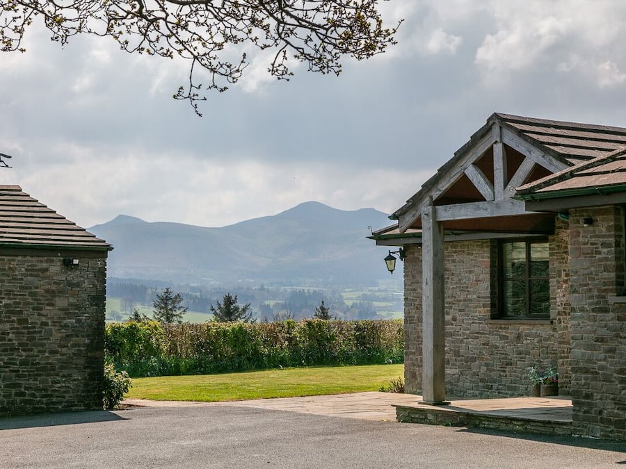 A stone building with a covered porch and a view of mountains in the background.