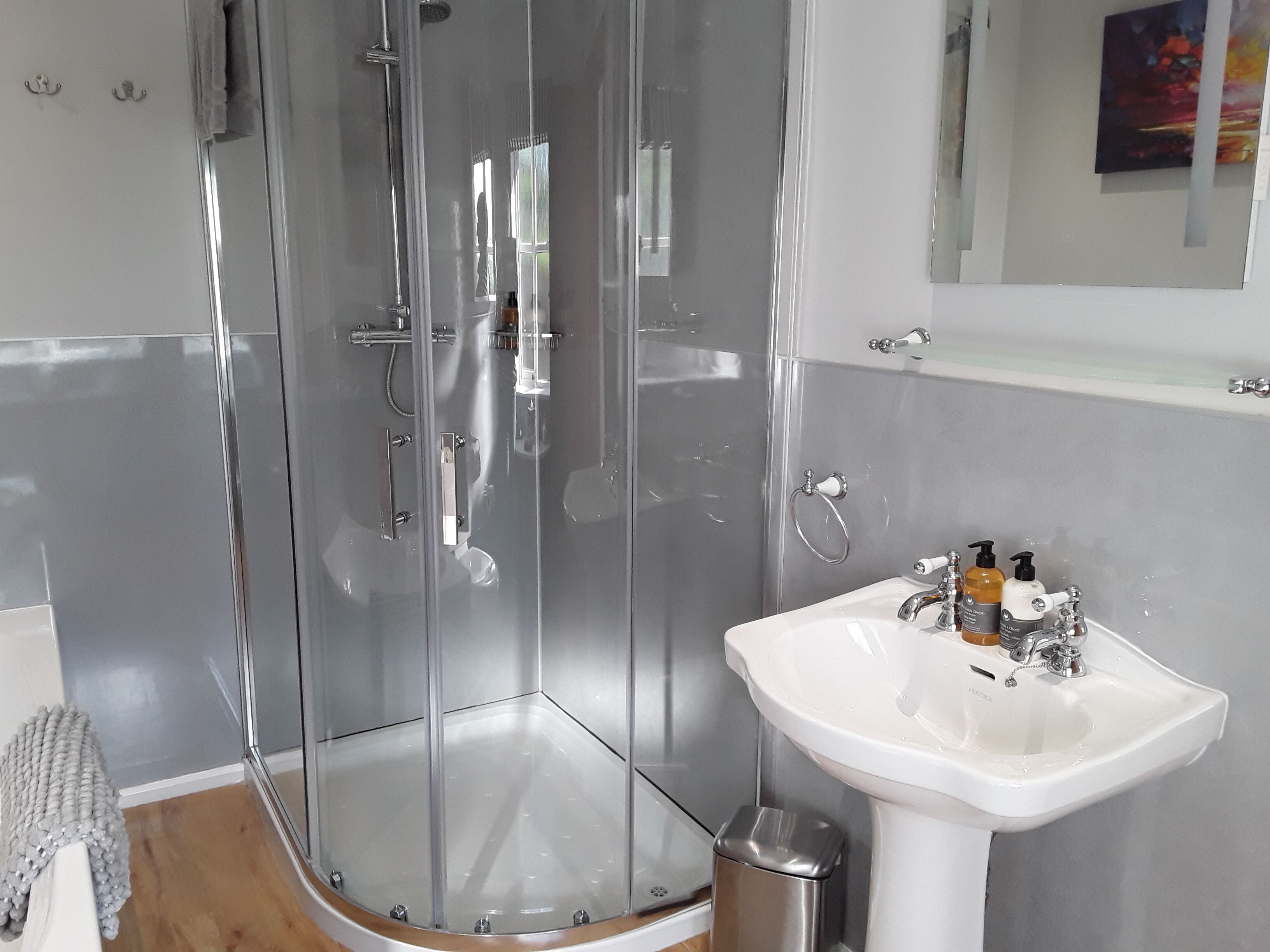Een moderne badkamer met een douchecabine van glas, een witte wastafel en een kleine prullenbak.