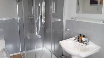 Un baño moderno con ducha de vidrio, lavamanos blanco y un pequeño cubo de basura.