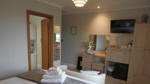 Un dormitorio con cama, cómoda, tocador con espejo y televisor montado en la pared.