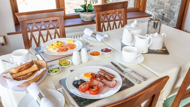 Un desayuno servido con platos de huevos, tocino y tomates, junto con pan y salsas.