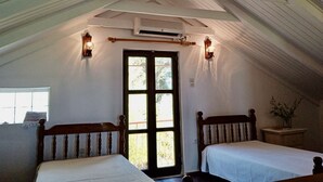 Un dormitorio con dos camas, una ventana, un equipo de aire acondicionado y una lámpara fijada a la pared.
