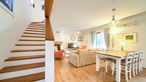 A modern living room with a wooden staircase, a sofa, a dining table with chairs, and a TV. - Villa Rustika with a swimming pool and beautiful Seaview (Sužan (Krk))