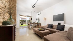 A modern living room with a brown sofa, a dining area with a table and chairs, and a view of a garden through the glass door. - Villa Luna with heated swimming pool & E-bikes (Županje (Krk))