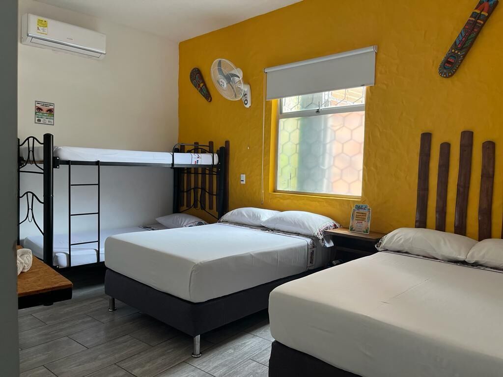 Une chambre de dortoir avec deux lits, un lit superposé, une fenêtre donnant sur un beau paysage et un ventilateur fixé au mur.