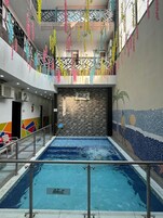 Una piscina interior con pared de azulejos y un mural, rodeada de decoraciones colgantes de colores.