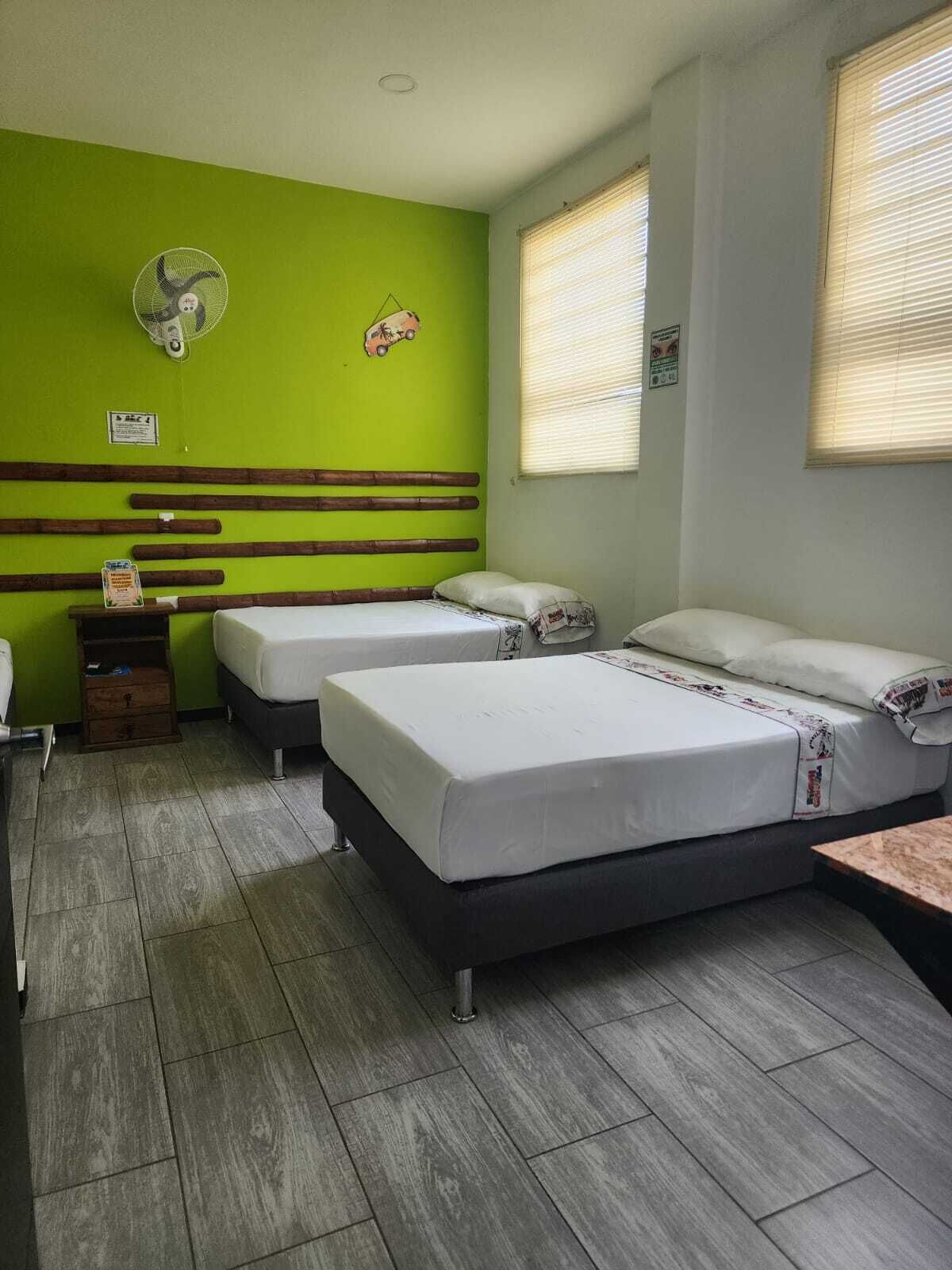 A room with two beds, a fan, and a small table.