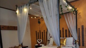 Een hemelbed met een baldakijn, witte en gouden accenten, een klein nachtkastje en een rode vloerkleed.