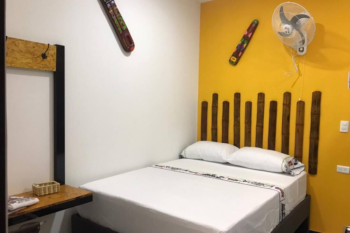 Ein Schlafzimmer mit einem Bett, einem Nachttisch, einem Wandventilator und einem dekorativen Gegenstand an der Wand.