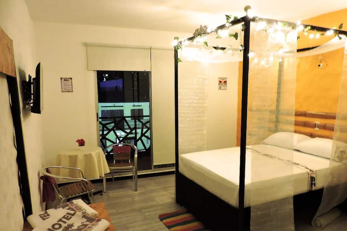Ein Zimmer mit Himmelbett, einem kleinen Tisch mit Stuhl, einem Fenster mit Blick auf ein Gebäude und Holzboden.