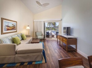 Ein Hotelzimmer mit Sofa, Sessel, Fernseher, Holztisch und einem Balkon mit Blick.