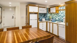 Eine kleine Küche mit Esstisch aus Holz, weißen Geräten und einer gefliesten Spritzschutzwand.