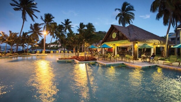 Ein Resort mit Pool, Palmen und einem Gebäude mit einem Reetdach.