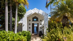 A white building with a triangular roof and a central door, surrounded by lush greenery and palm trees. - Waterfront Villa-Amazing View-Pool-Sea-Location#1 (Pointe Pirouette)