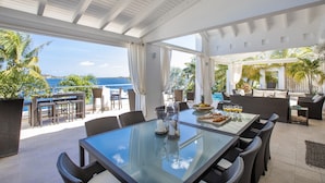A spacious outdoor dining area with a glass table, wicker chairs, and a view of the ocean. - Waterfront Villa-Amazing View-Pool-Sea-Location#1 (Pointe Pirouette)