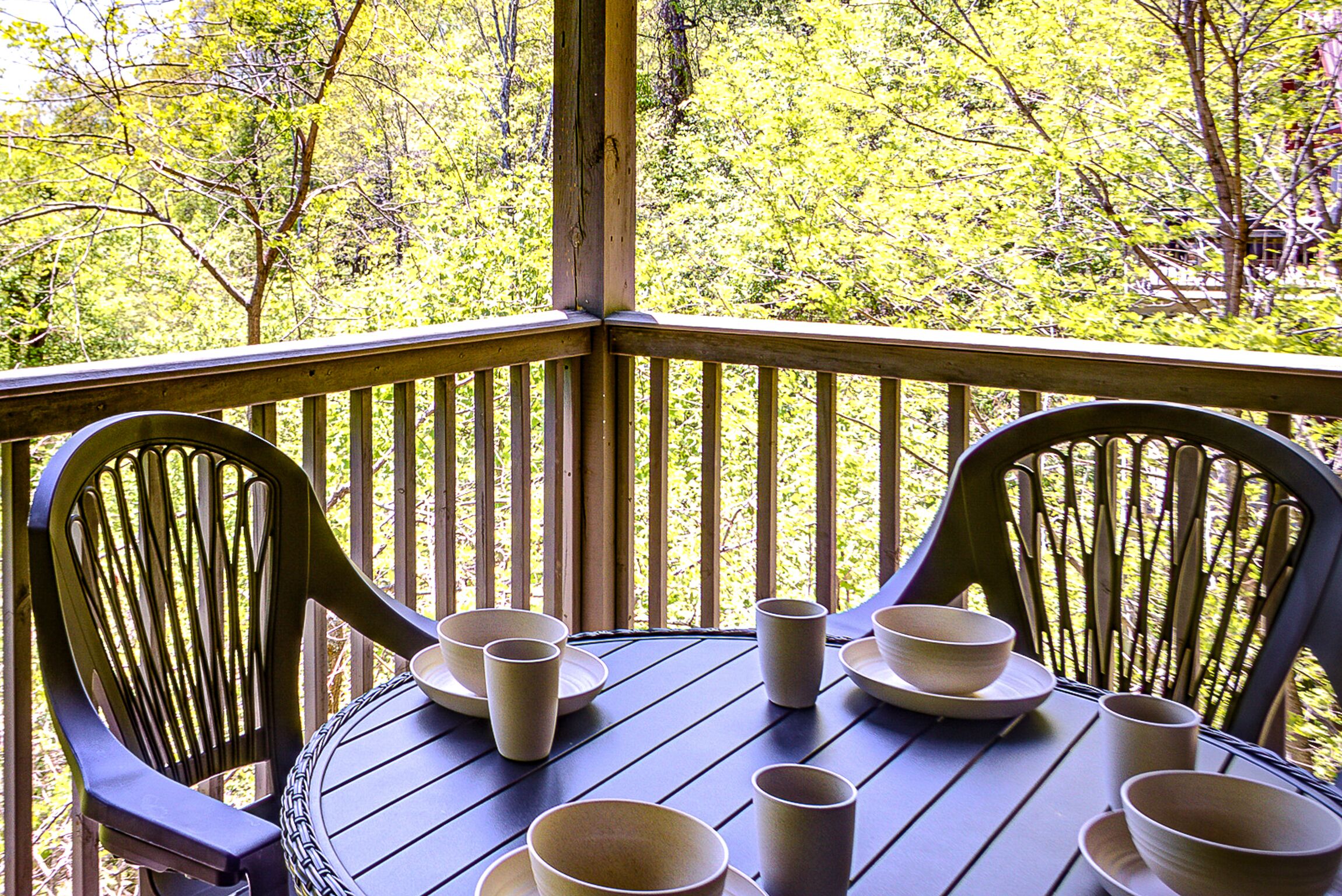 Una terraza de madera con una mesa dispuesta para comer, rodeada de sillas, con vistas a un área boscosa.