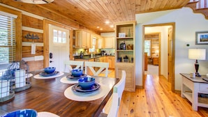 Un intérieur en bois comprenant un coin repas avec une table dressée, agrémentée de bols et d’assiettes bleus, une cuisine avec des placards en bois, et un couloir menant à une chambre.